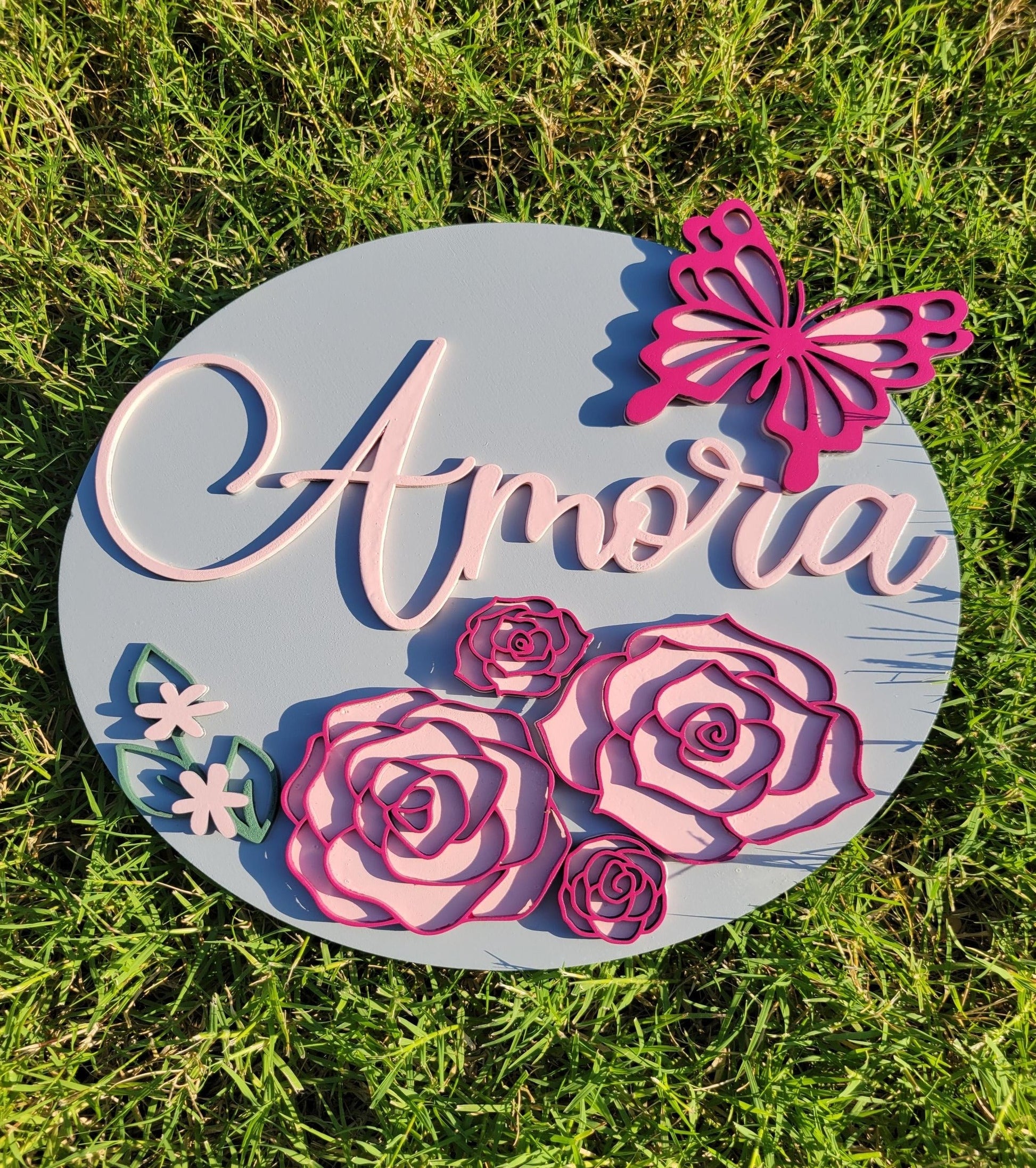 Two floral nursery signs. One gray background with two toned pink flowers and butterfly