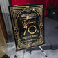 Decorative birthday sign with gold text on a black background, placed in front of a red drape and stage