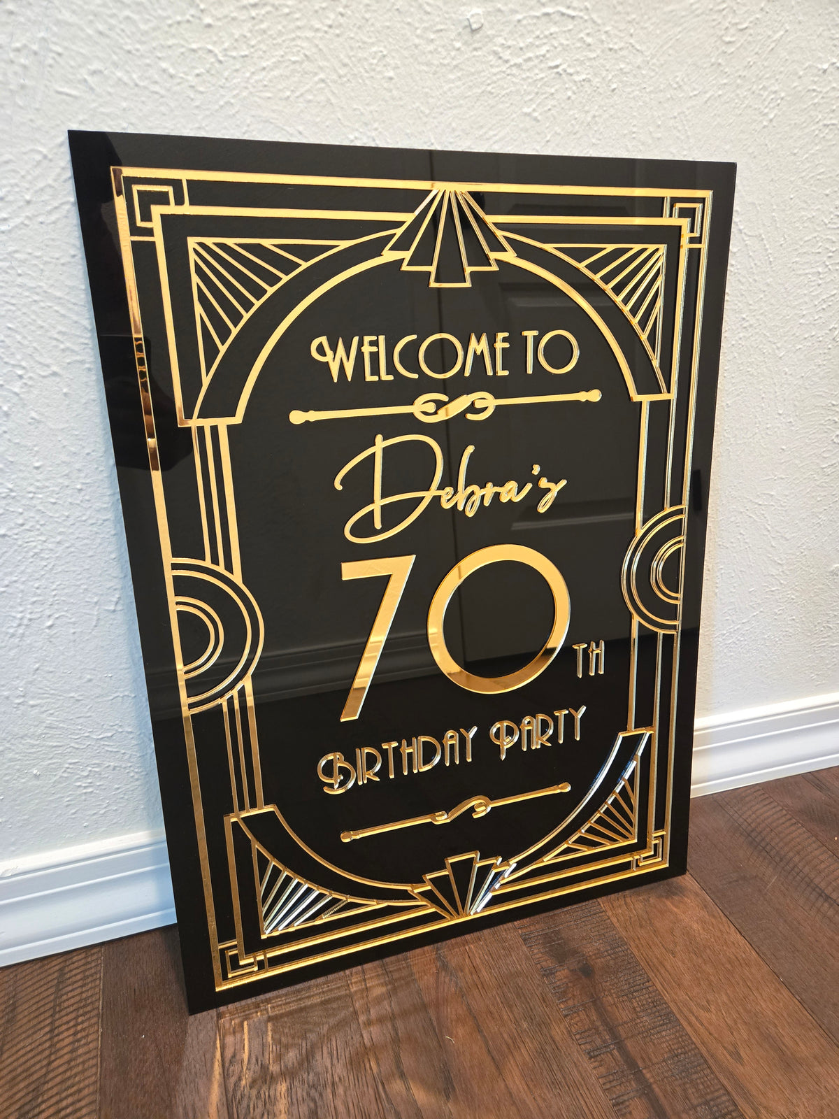 Decorative birthday party sign with gold text on a black background, leaning against a wall.